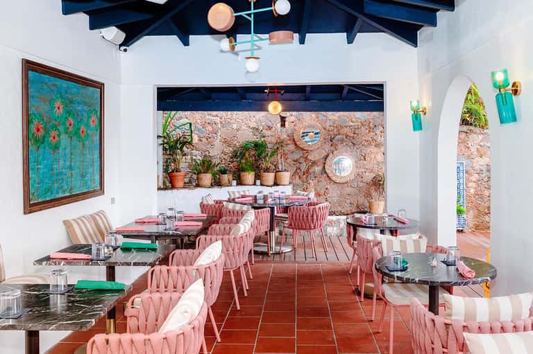 Colorful outdoor restaurant with pink chairs, cork walls, and Mediterranean architectural details