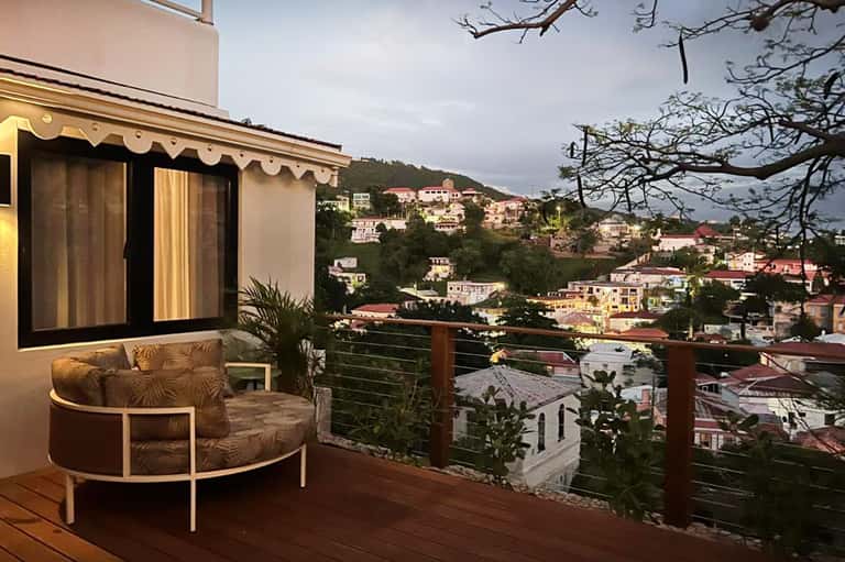 Resort balcony with modern seating overlooking hillside town with red-roofed buildings and tropical vegetation