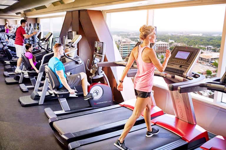 High-rise gym with treadmills and exercise bikes overlooking cityscape through floor-to-ceiling windows