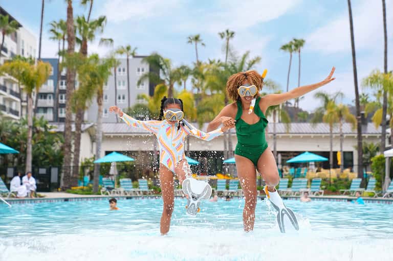 Mother and child jumping into resort pool with palm trees and buildings