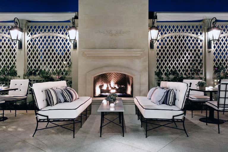 Elegant outdoor fireplace lounge with white cushioned seating and lattice blue backdrop
