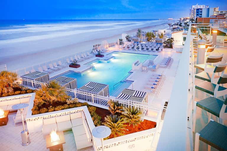 Beachfront resort pool deck at dusk with ocean view and lounge chairs