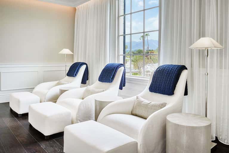 Spa relaxation lounge with white upholstered recliners, blue blankets, large windows, mountain views