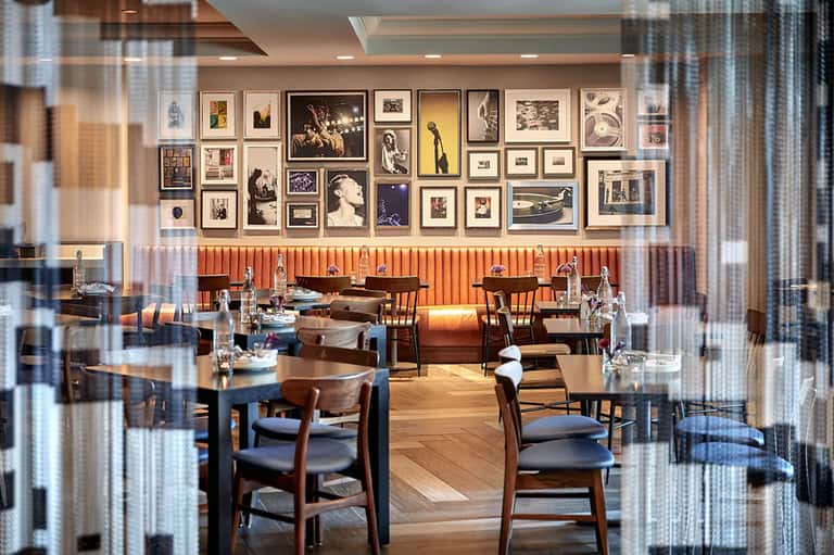 Modern restaurant interior with wood and metal furnishings, gallery wall of framed artwork, and contemporary design