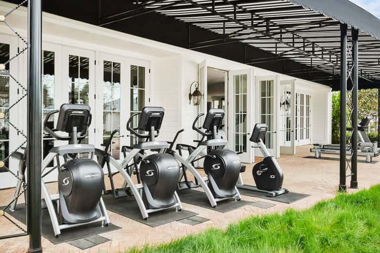 Outdoor fitness area with elliptical machines under pergola near white building