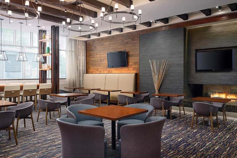 Contemporary hotel lounge with fireplace, pendant lights, wood brick accent wall, and seating areas