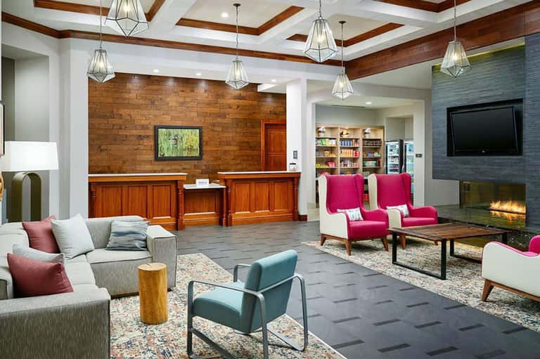 Modern hotel lobby with wood beams, fireplace, colored armchairs, and reception desk