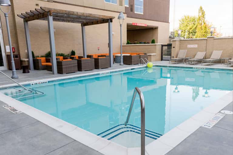 Urban hotel pool with pergola seating area featuring orange cushions