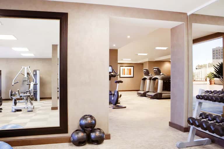 Contemporary fitness center with exercise equipment, mirrors, and neutral beige tones