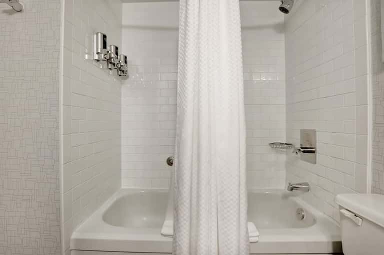 Clean white bathroom with dual sinks, subway tile walls, shower area, and chrome fixtures