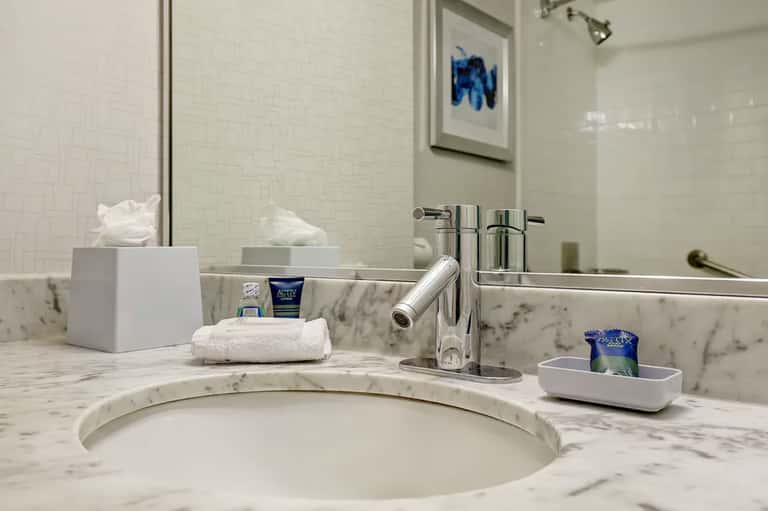 Marble bathroom vanity with circular sink, chrome faucet, mirror, and white toiletries