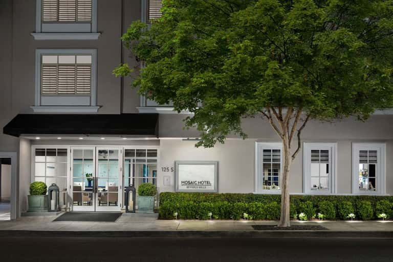 Mosaic Hotel storefront with clean modern facade, black awning, glass doors, landscaped hedges, and street-level entrance