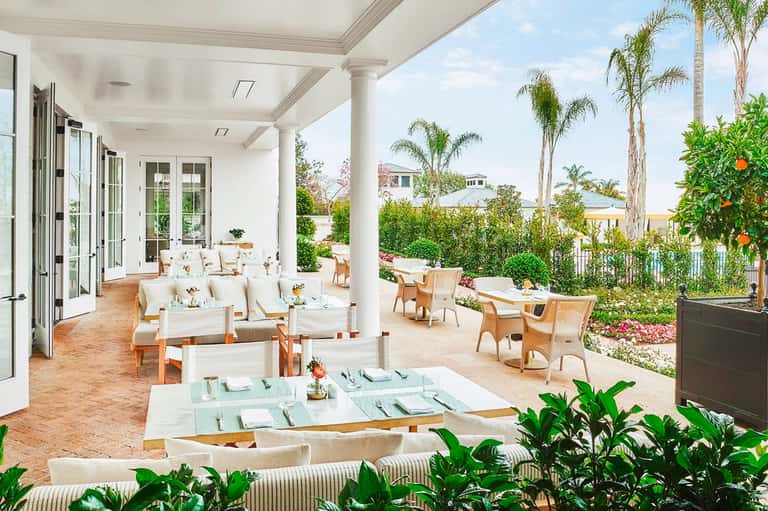 Elegant outdoor dining and lounge area with white columns, comfortable seating, and manicured gardens