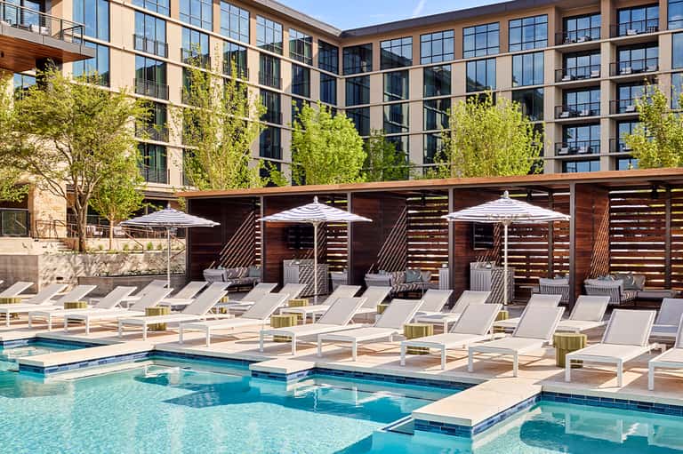Contemporary courtyard pool with white lounge chairs, umbrellas, and multi-story apartment building