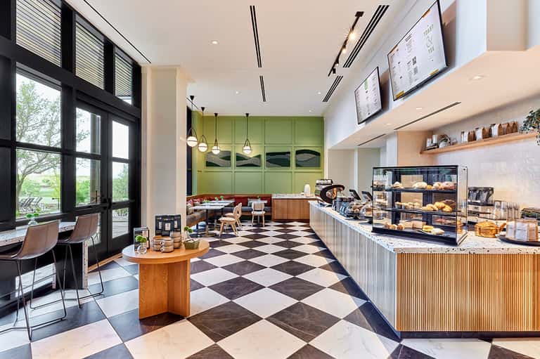 Bright cafe interior with checkered floor, green kitchen, pendant lights, and pastry display