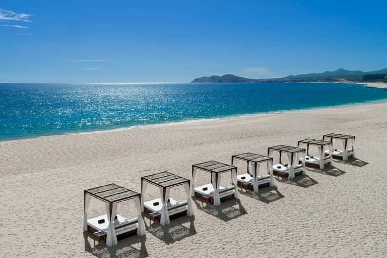 Row of white beach cabanas with black canopies on pristine sand overlooking turquoise ocean