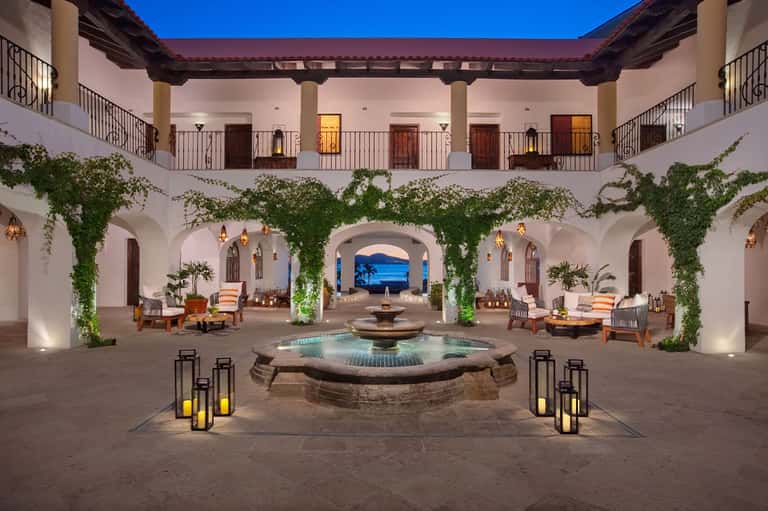 Spanish colonial courtyard at dusk with central fountain, ivy-draped columns, and ocean view arch