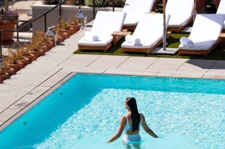 Woman swimming in bright turquoise pool with white loungers and rolled towels poolside