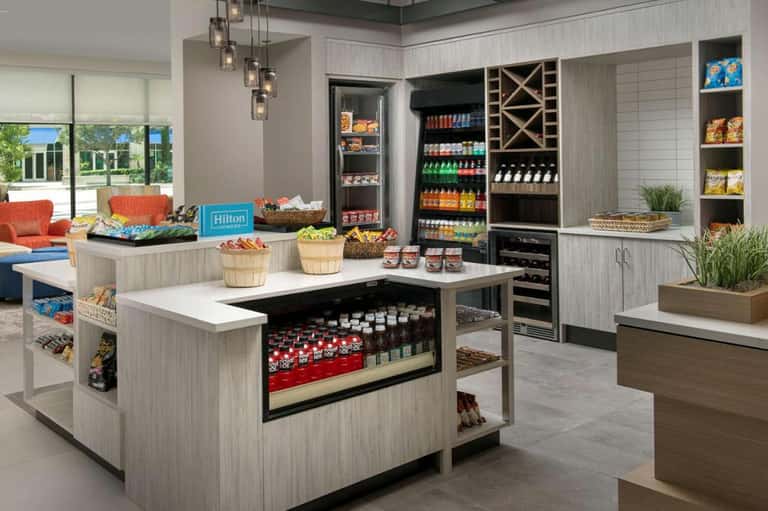 Modern hotel pantry with refrigerated displays, snack stations, island counter, and lounge seating