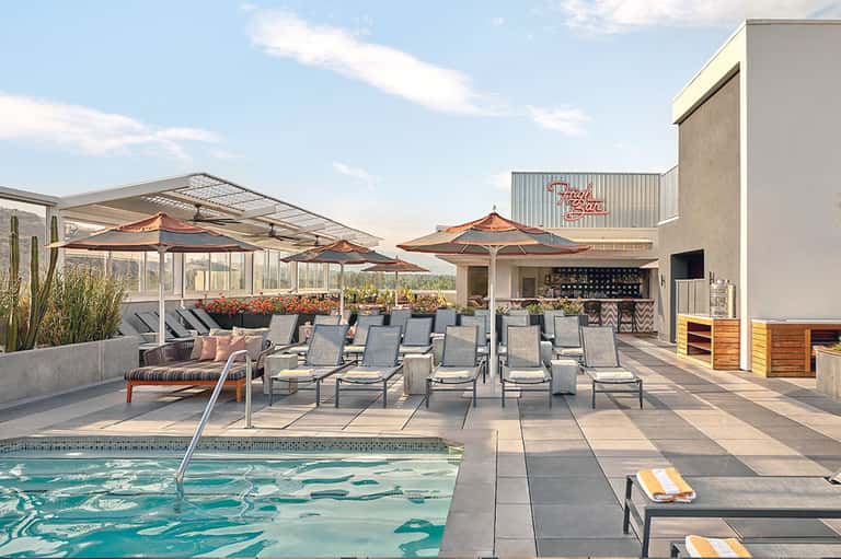 Rooftop pool deck with lounge chairs, umbrellas, and modern resort building