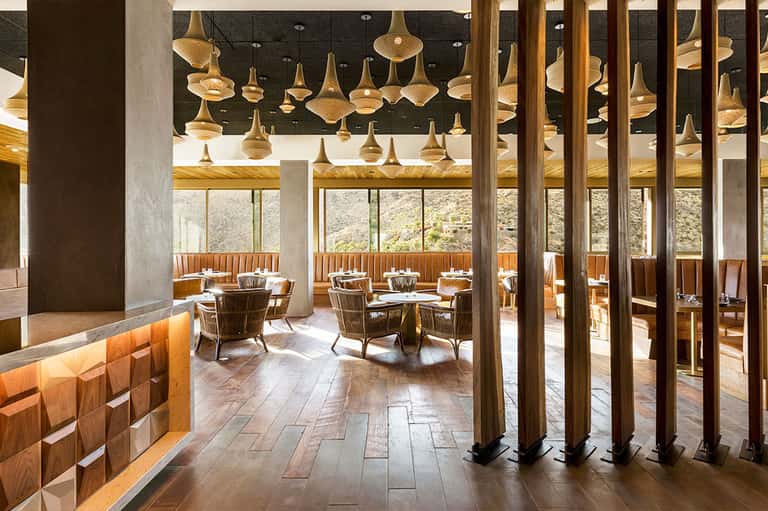 Upscale restaurant interior with brass pendant lights, wooden seating, and scenic outdoor views
