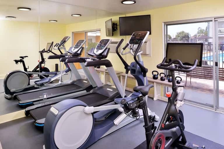 Bright fitness facility with exercise equipment, stationary bikes, and access to pool deck