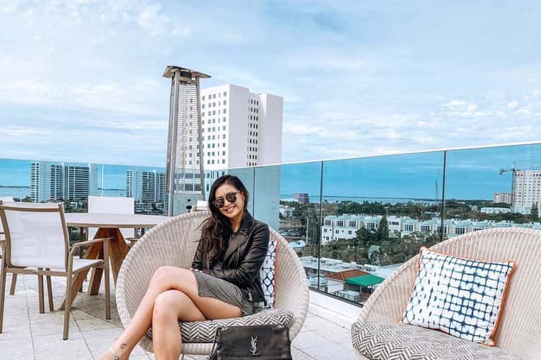 Woman in sunglasses on rooftop terrace with coastal city views and high-rise buildings