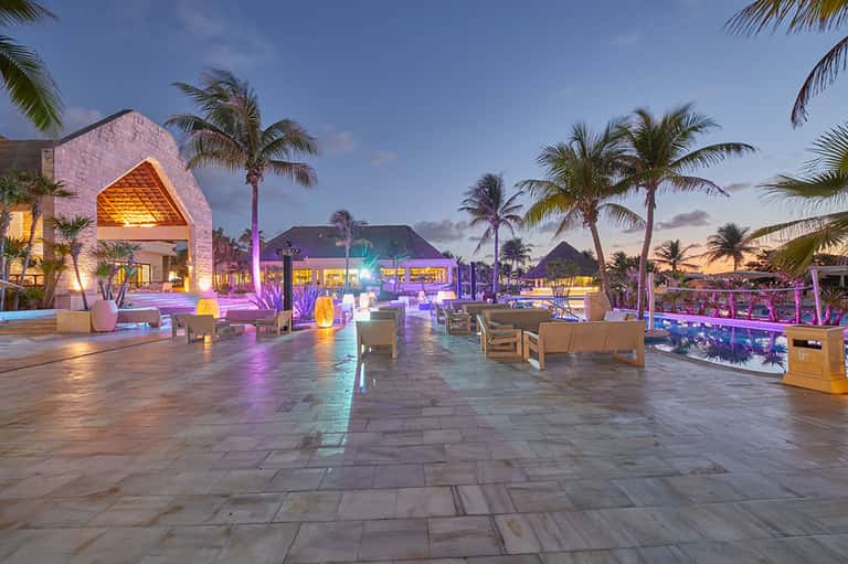 Resort courtyard at dusk with modern architecture, palm trees, and colorful ambient lighting