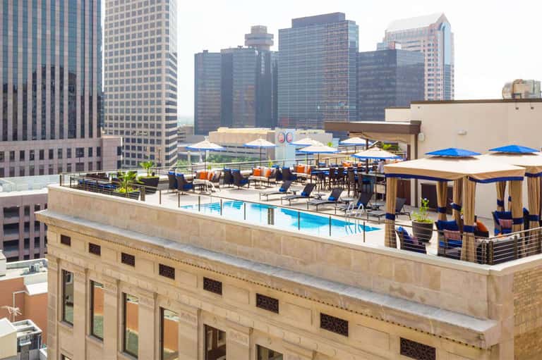 Rooftop pool deck with blue umbrellas and city skyline views at an urban high-rise hotel.
