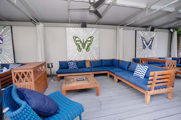 Covered patio lounge with blue cushioned wooden seating, butterfly art panels, and wooden table
