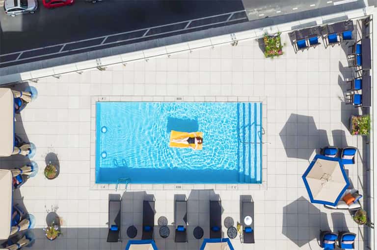 Aerial view of rectangular swimming pool with person on yellow float, surrounded by lounge chairs and white deck