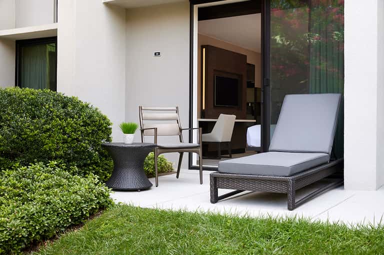 Modern patio with black rattan lounger, chair, side table, and manicured hedges