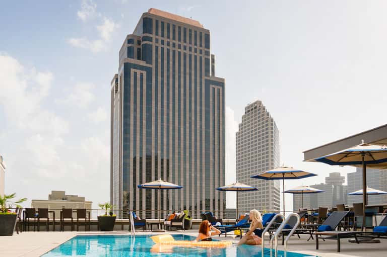 Rooftop pool with city skyline views, lounge chairs, and yellow umbrellas at urban hotel