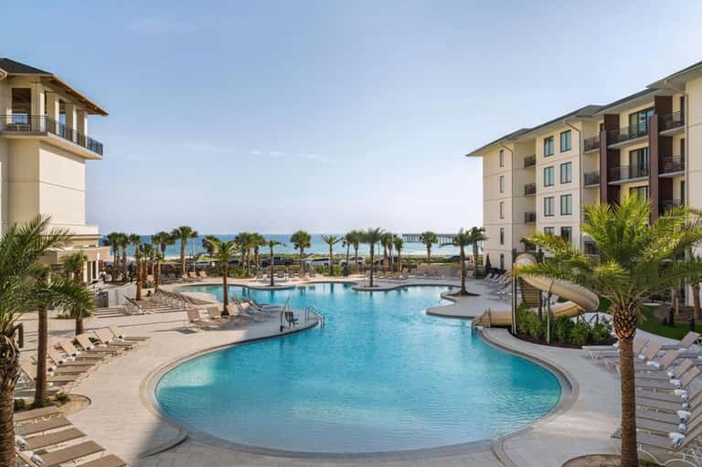 Large curved resort pool with turquoise water, palm trees, and multi-story hotel buildings
