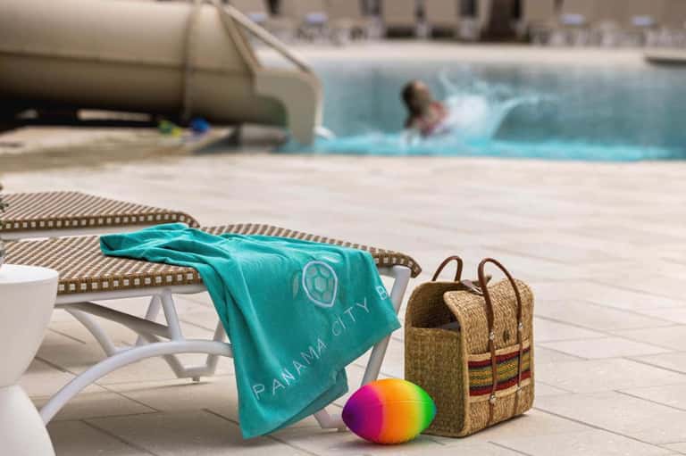 Poolside scene with colorful beach towel, straw bag, and beach ball on lounge chair