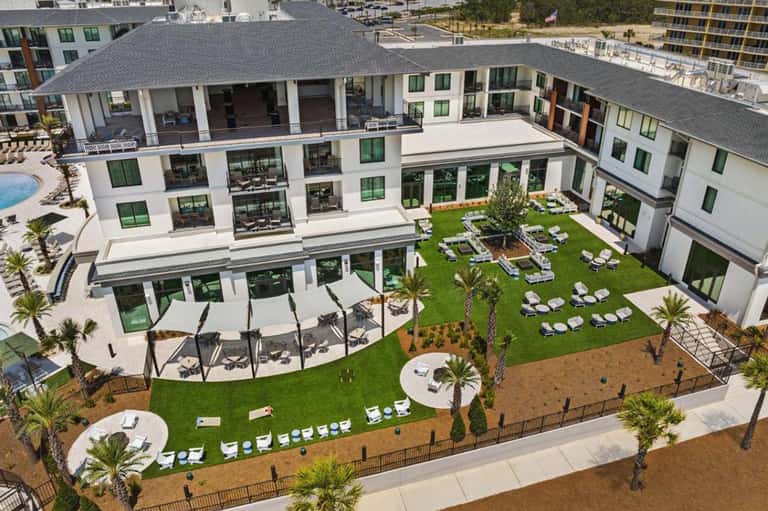 Beachfront resort courtyard with green lawn, lounge chairs, and modern white buildings