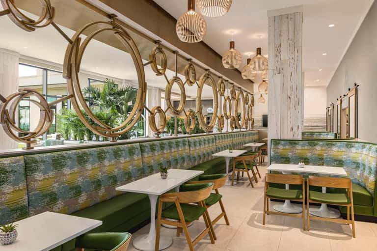 Modern restaurant interior with gold circular mirrors, green booth seating, and pendant lighting