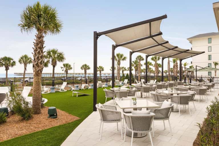 Oceanfront dining terrace with pergolas, wicker chairs, white tables, palm trees, ocean view