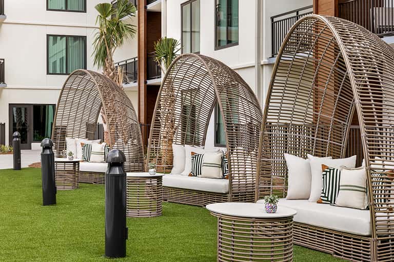 Modern resort outdoor lounge area with three large woven egg-shaped chairs and white cushions on grass