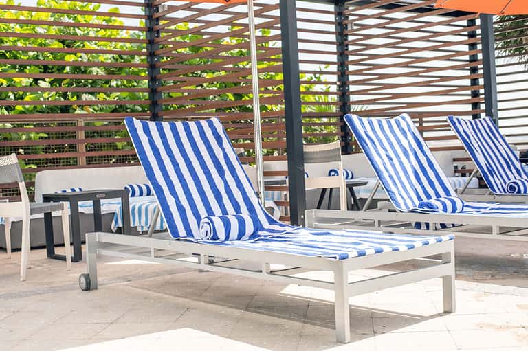 Blue and white striped lounge chairs on sunny patio with horizontal slat pergola overhead