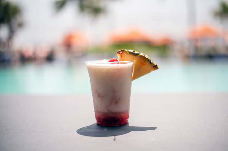 Tropical cocktail with pineapple garnish on sandy beach with pool in background