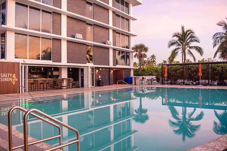 Contemporary resort pool at dusk with modern building and Salty Siren bar