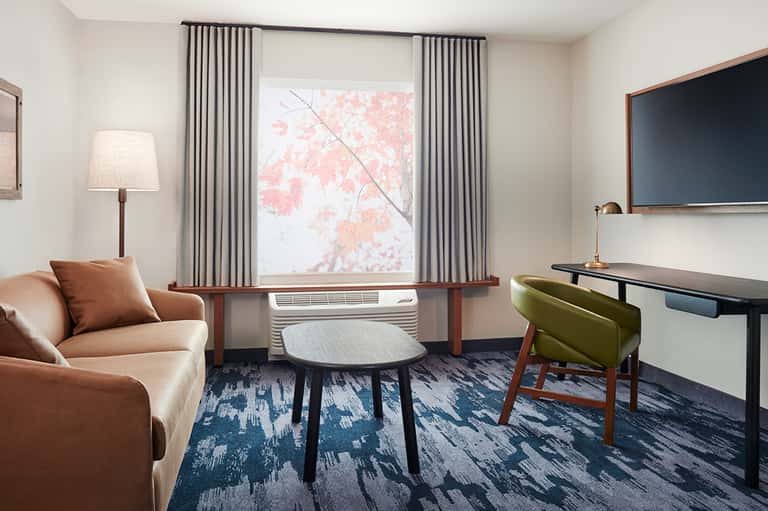 Contemporary hotel suite with tan leather sofa, mid-century desk, and blackout curtains over window