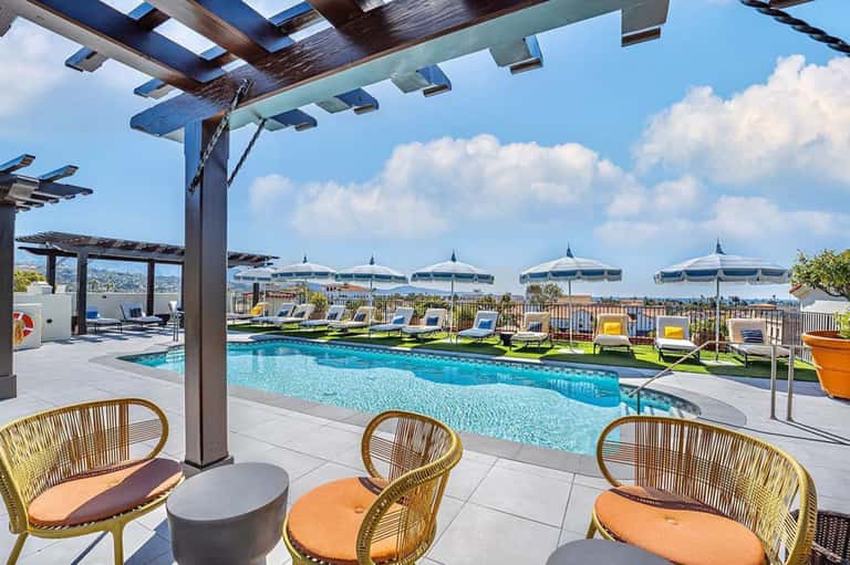 Upscale poolside lounge with pergola, woven chairs, white umbrellas and mountain views