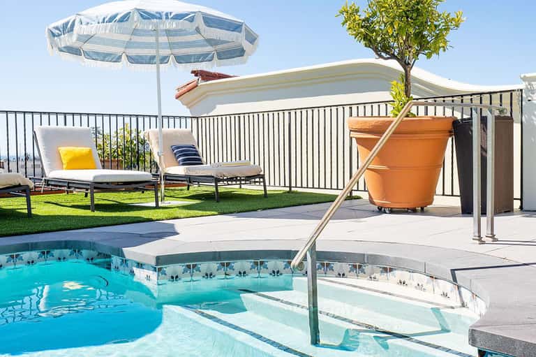 Resort pool and spa area with lounge chairs, umbrella, white railing, and bright turquoise water