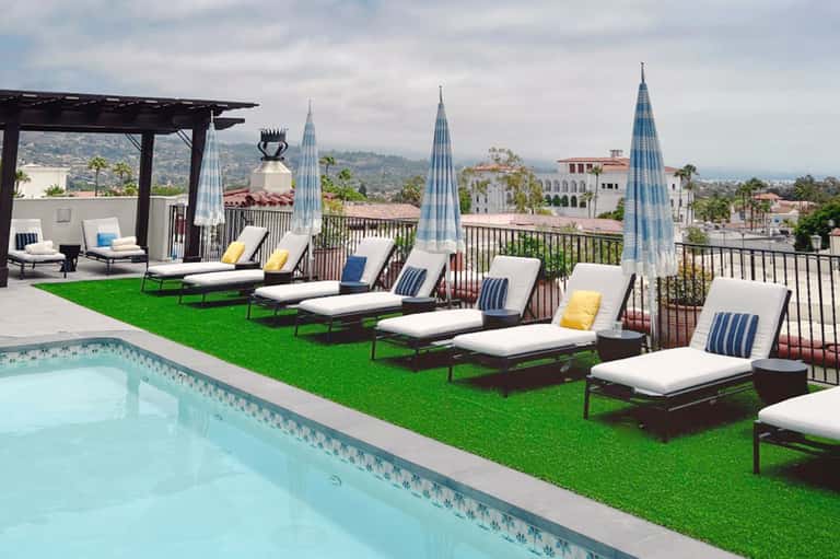 Rooftop pool overlooking hillside with lounge chairs on artificial turf and city skyline