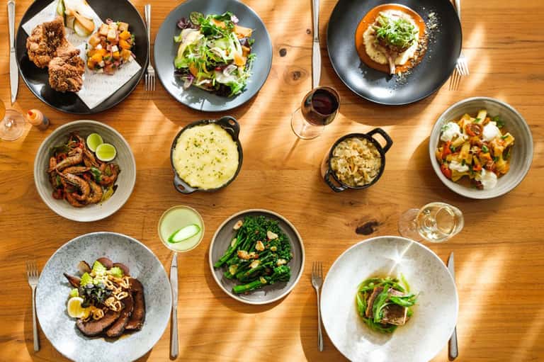 Fine dining overhead view with multiple plated dishes and wine glasses on wooden table