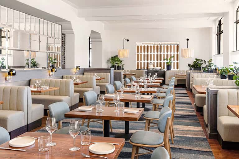 Contemporary dining room with beige banquette seating, wood tables, pendant lights, and minimalist decor