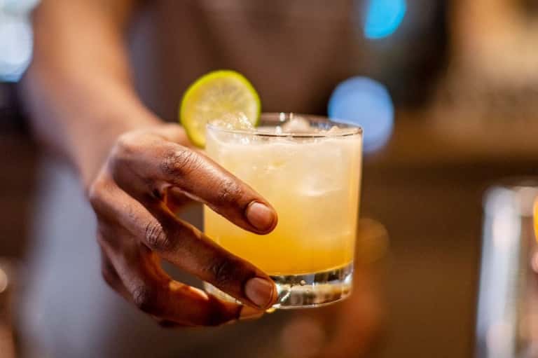 Close-up of amber cocktail with lime garnish held in hand