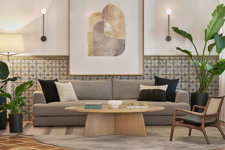 Modern lounge interior with gray sofa, decorative artwork, patterned tile accent wall, and potted plants